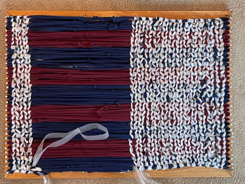 Nail loom with partially completed rug in blue and Burgundy with white weft