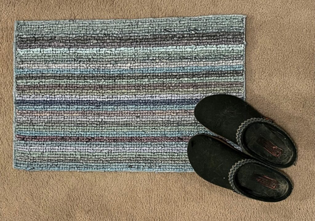 Completed rug with multiple colored stripes and shoes to show size